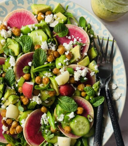 A beautifully arranged spring salad on a platter, with a jar of fresh herb dressing on the side, ready to serve.