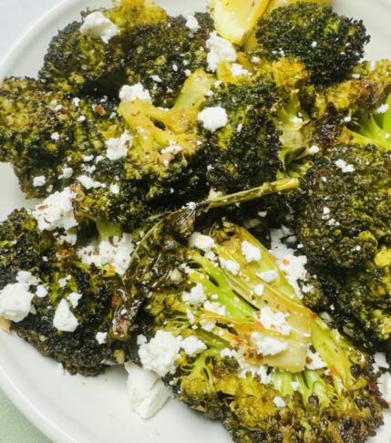 Roasted broccoli in a serving bowl, topped with crumbled feta and fresh lemon slices for a vibrant Mediterranean touch.