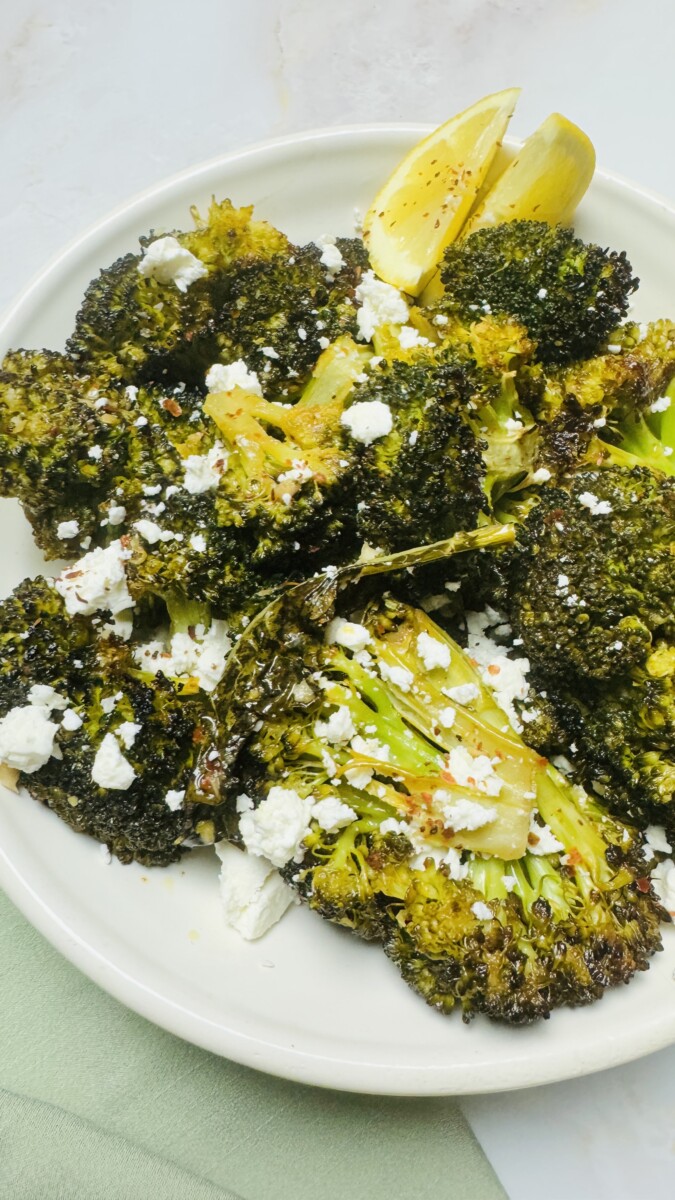 Roasted broccoli in a serving bowl, topped with crumbled feta and fresh lemon slices for a vibrant Mediterranean touch.