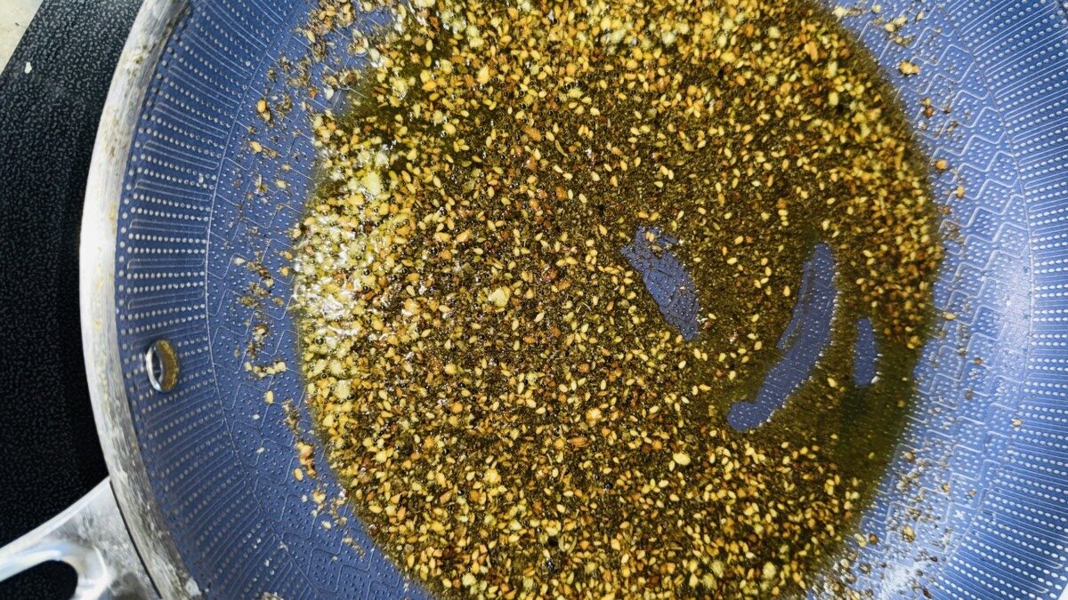 Garlic and za’atar sizzling in olive oil in a skillet, releasing aromatic flavors."