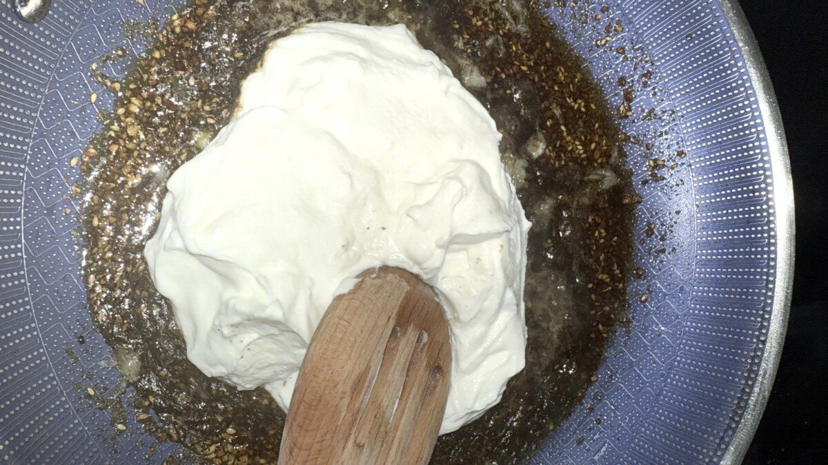 Greek yogurt being stirred into a skillet with sautéed za’atar and garlic.