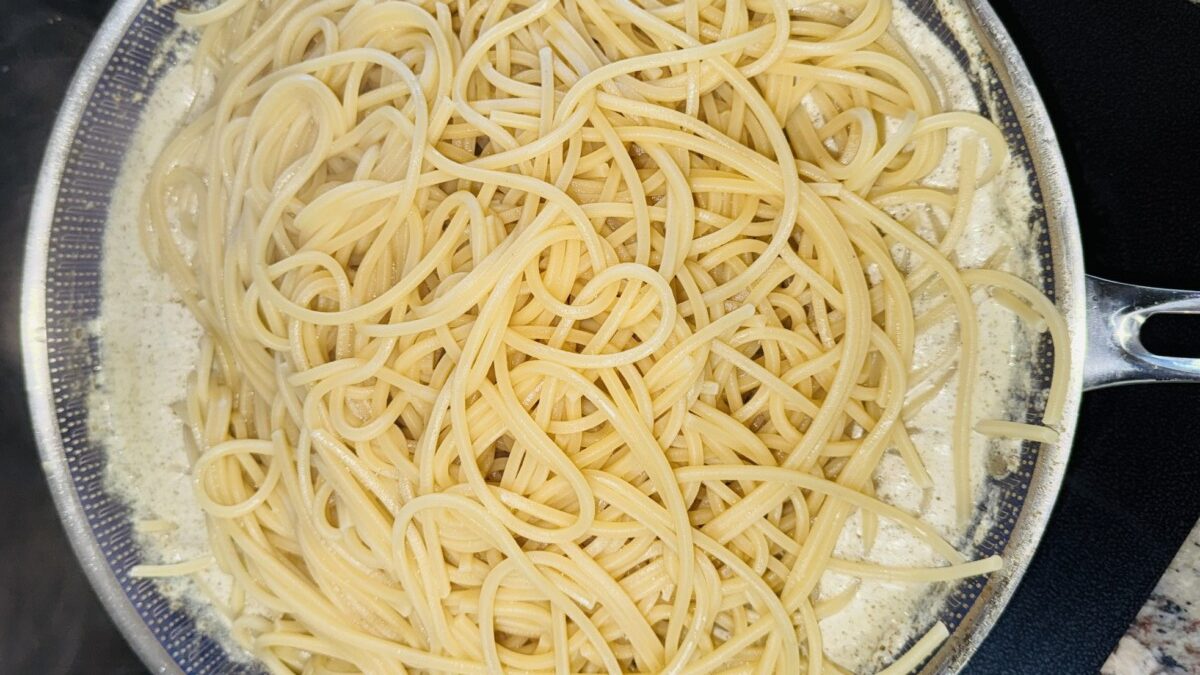 Cooked pasta being tossed into a creamy za’atar yogurt sauce in a skillet.