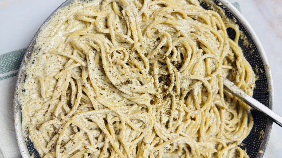 Cooked pasta being combined into a creamy za’atar yogurt sauce in a skillet.