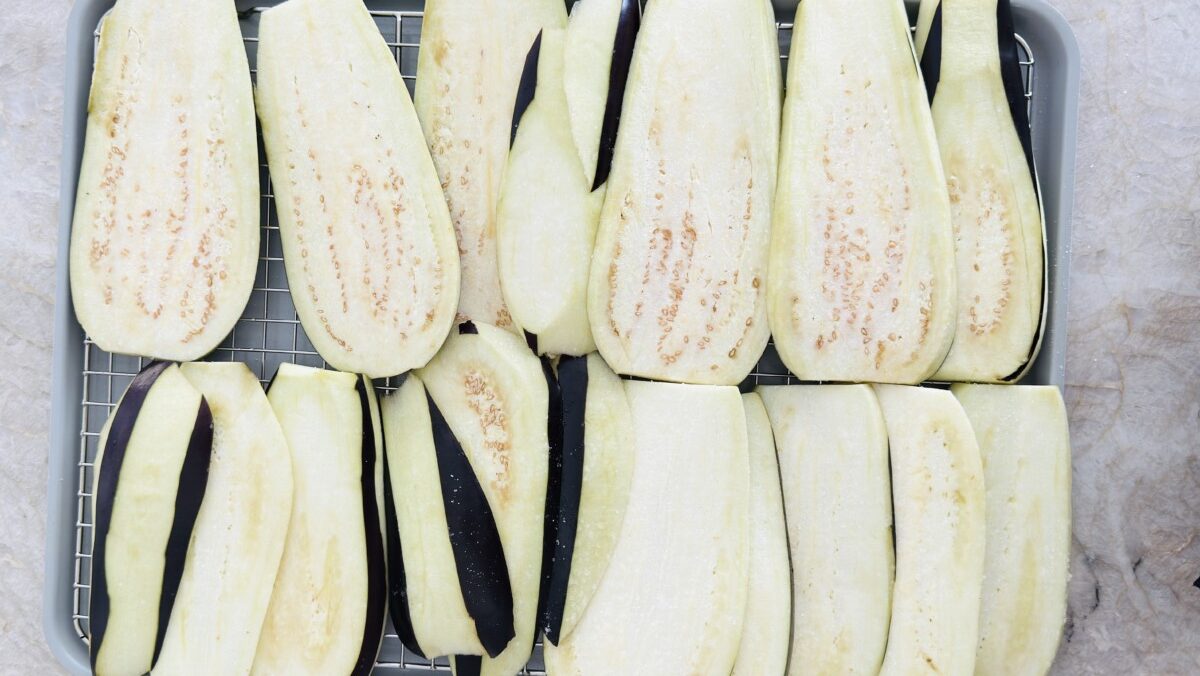 Sliced eggplant sprinkled with salt resting on a tray to draw out excess moisture before roasting.