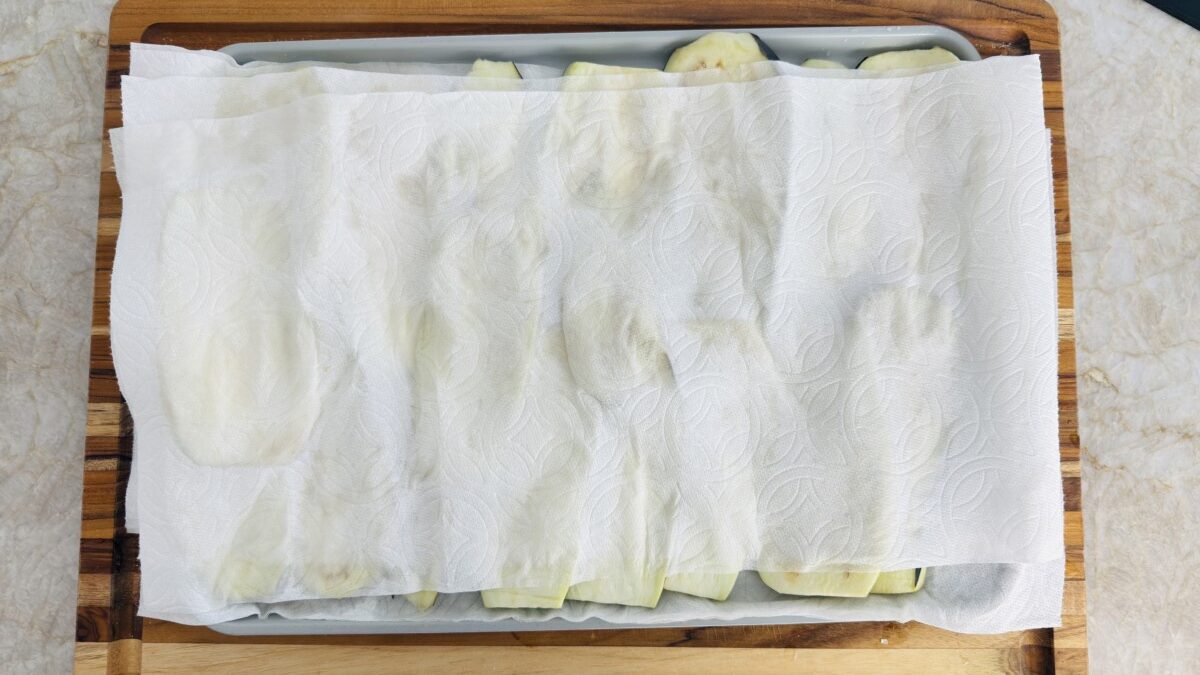 Eggplant slices being rinsed and patted dry with paper towels after salting.