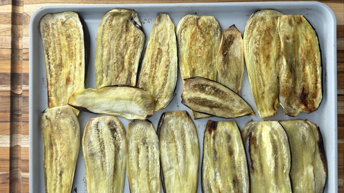 Roasted eggplant slices cooling on a tray after baking, ready for rolling.
