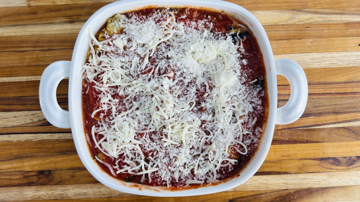 Shredded mozzarella and parmesan cheese layered over sauced eggplant rollatini before baking.