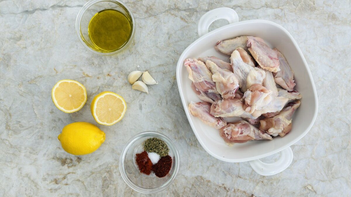 Overhead view of fresh ingredients for baked chicken wings, including lemon, garlic, spices, olive oil, and Greek yogurt.
