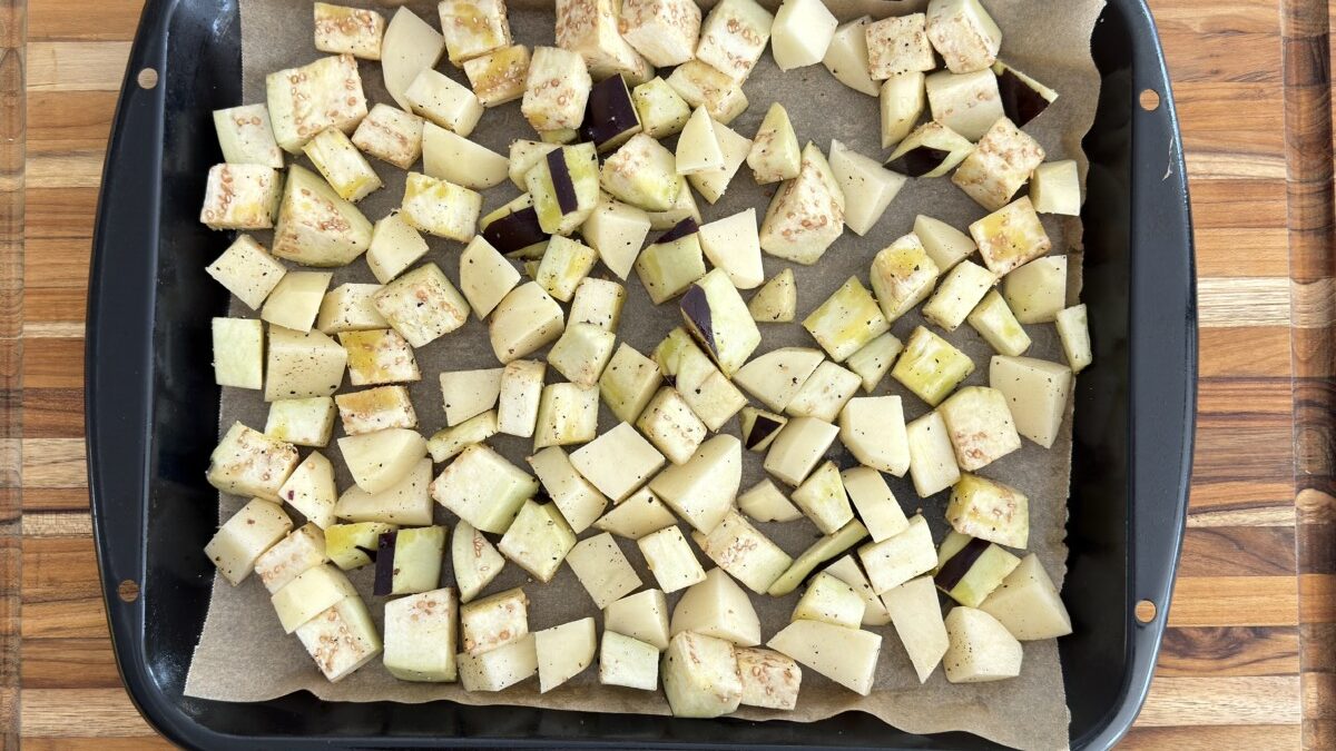 Cubed potatoes and eggplant arranged on a baking tray, drizzled with olive oil, ready to roast.