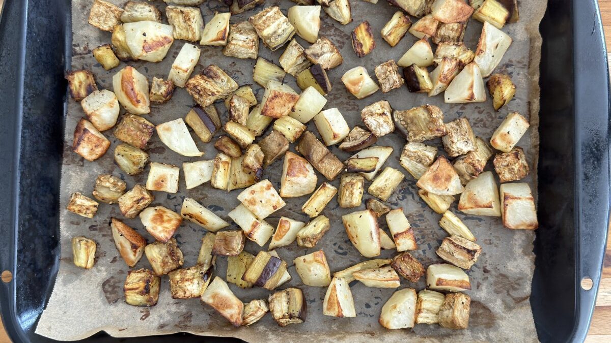 Golden roasted eggplant and potatoes on a baking tray, caramelized and tender.