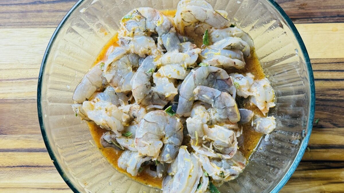 Shrimp marinating in a bowl with Greek spices and herbs.