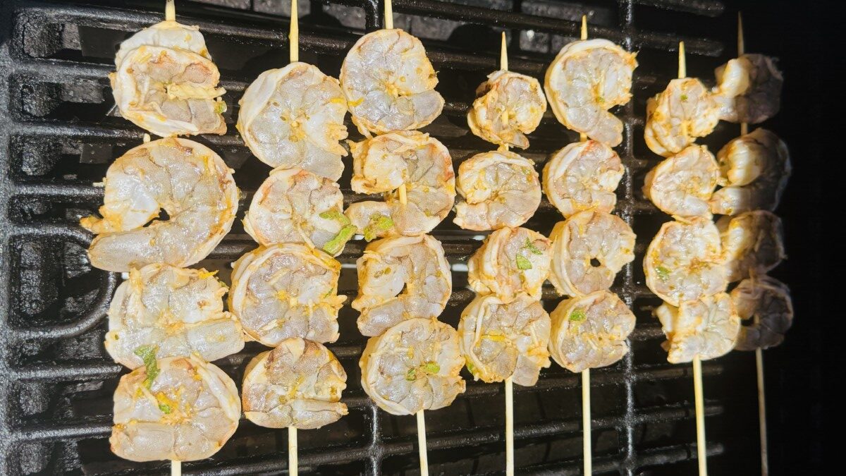 Shrimp skewers sizzling on a hot grill with char marks forming.