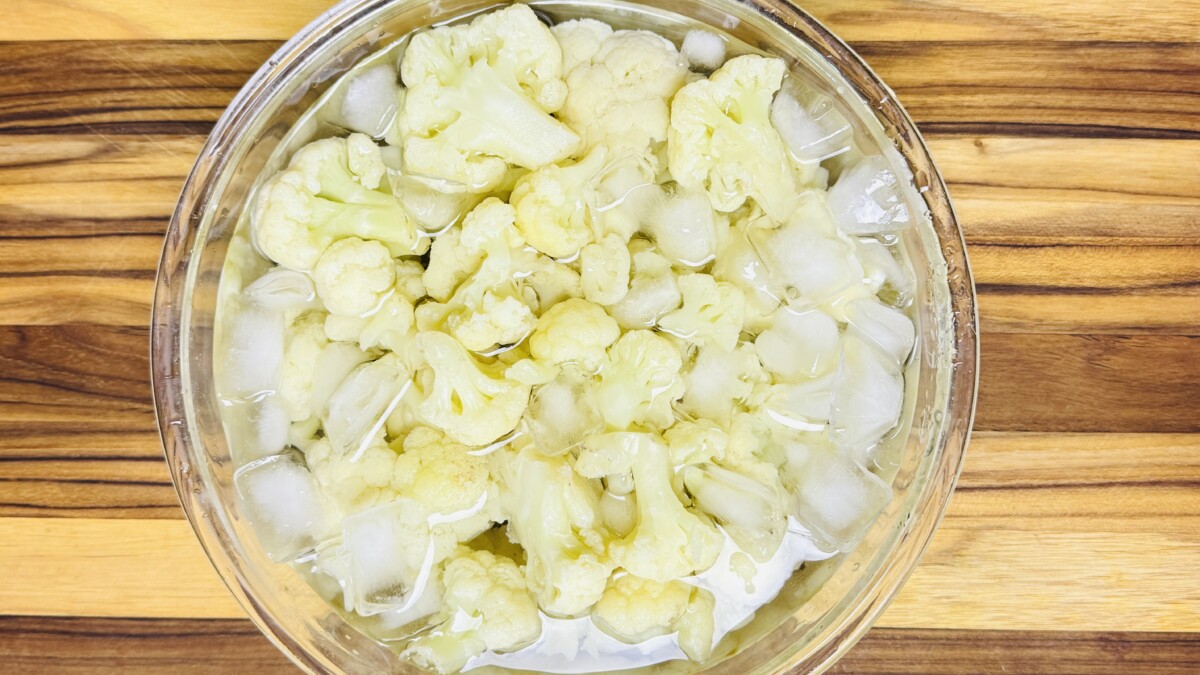 Boiled cauliflower florets submerged in a bowl of ice water to stop cooking and preserve texture for fritter recipe.