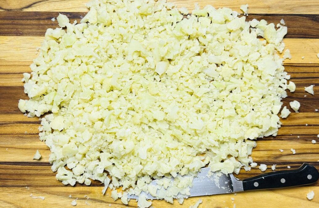 Cauliflower florets being chopped into small pieces on a cutting board for fritter preparation.