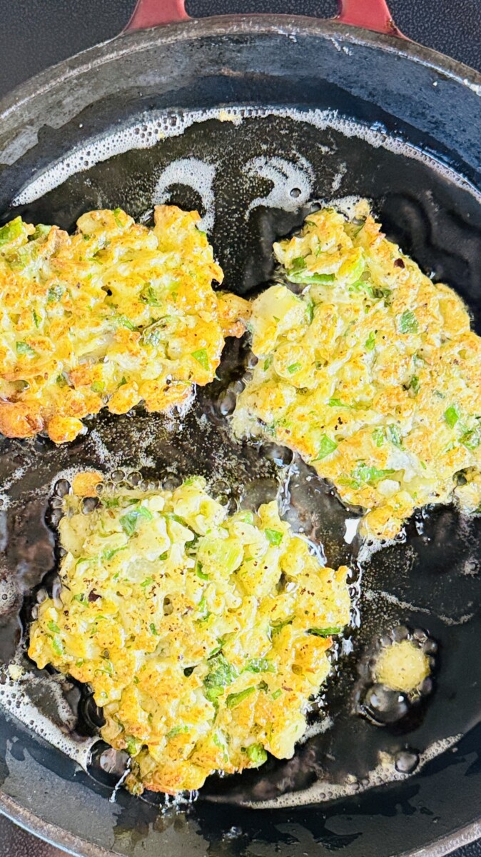 Cauliflower fritters sizzling in a skillet with oil, shallow-fried to golden perfection.