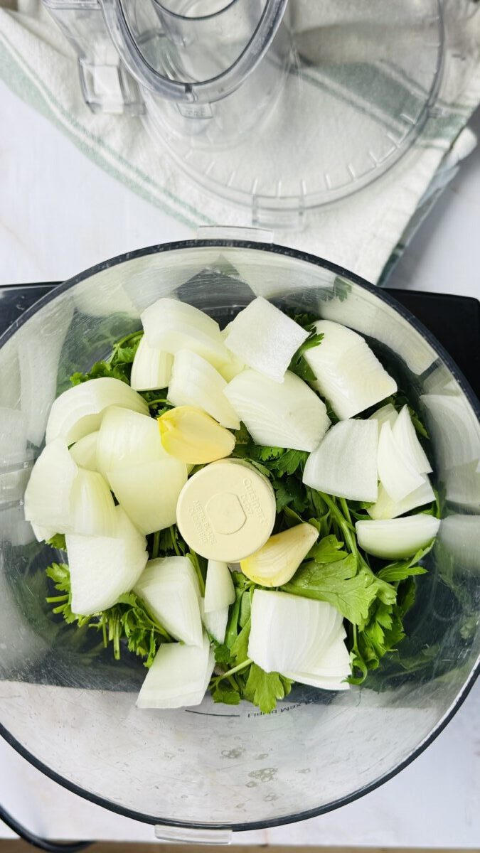 Fresh parsley, cilantro, garlic, and onions in a food processor, ready to be chopped for Arayes filling.