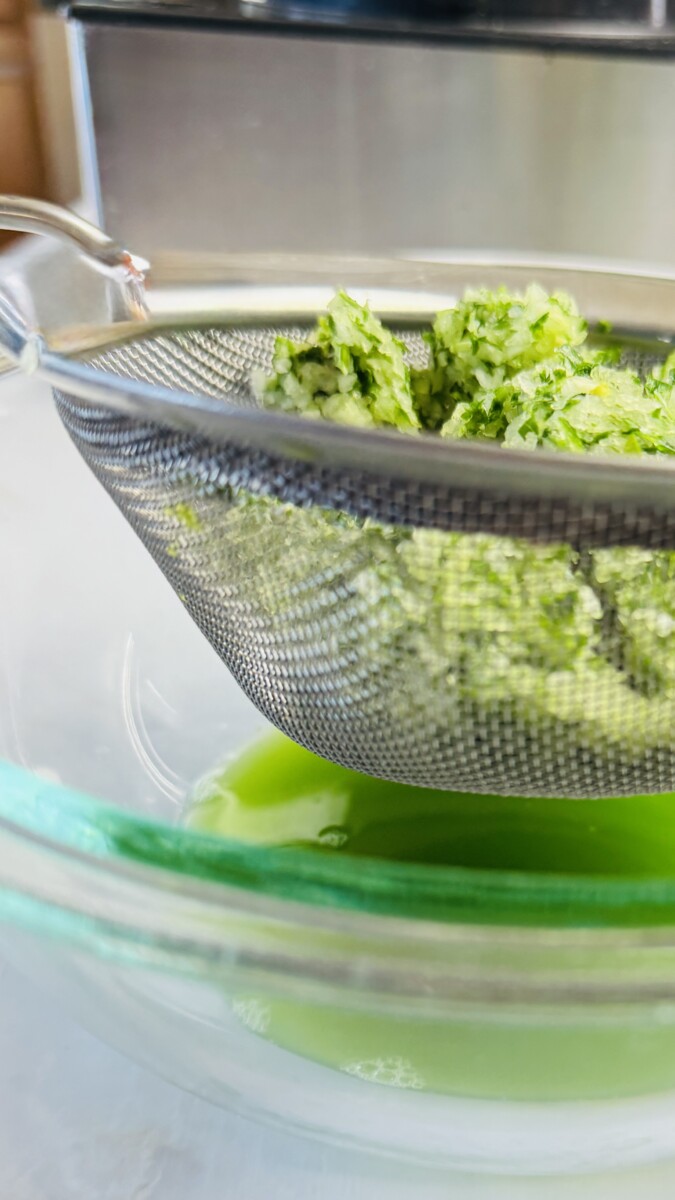 Chopped onion, parsley, cilantro, and garlic mixture being strained in a fine mesh strainer lined with paper towels to remove excess water.