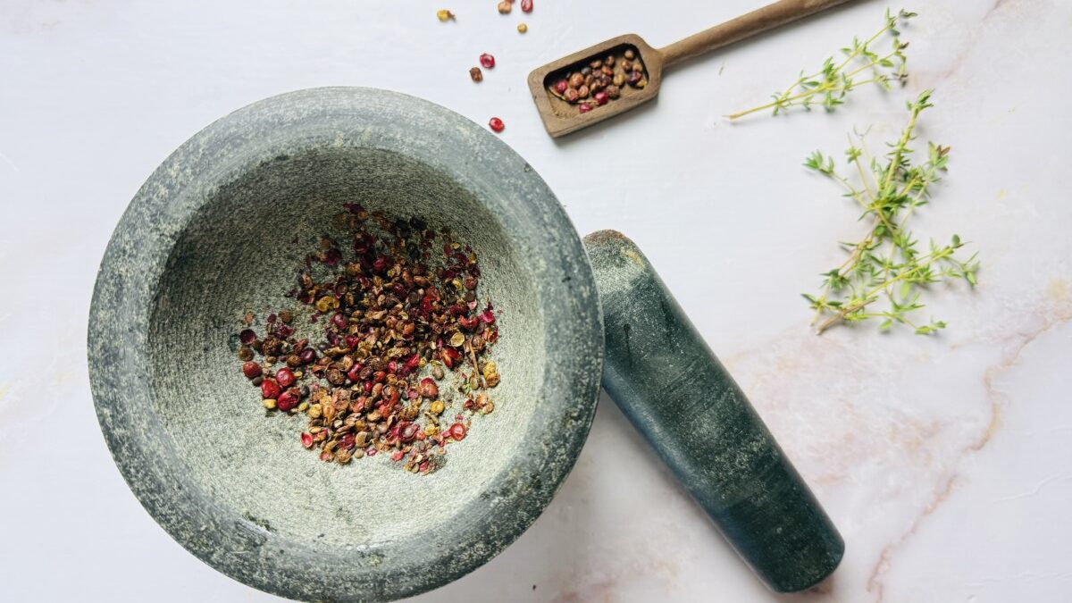 Whole sumac berries being crushed in a mortar and pestle for use in pickled red onion recipe.