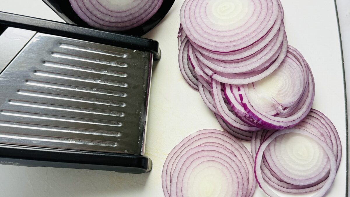 Red onions being thinly sliced using a mandoline slicer for quick pickling.