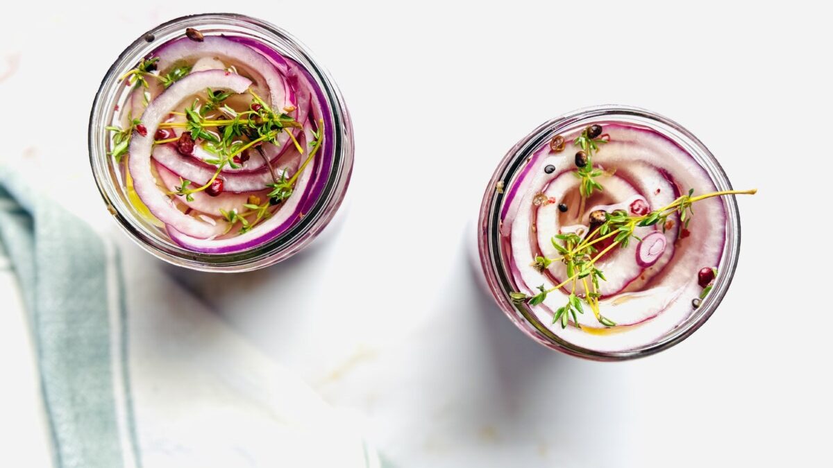 Two jars of freshly pickled red onions cooling on the counter after being filled with hot brine.