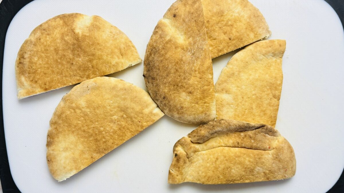 Thick pita bread cut in half and arranged on a cutting board, ready to be filled for Arayes.
