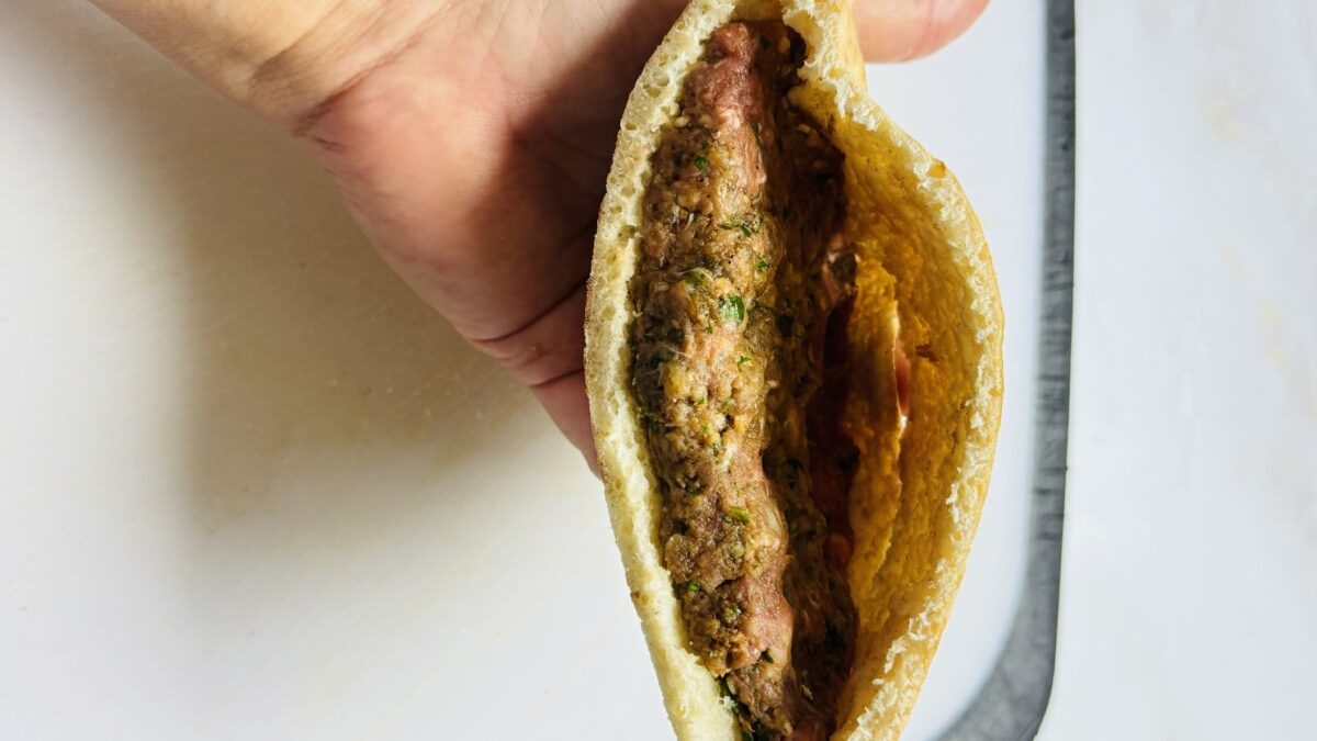 Pita bread half stuffed with an even layer of seasoned ground meat, ready to be grilled for Arayes.