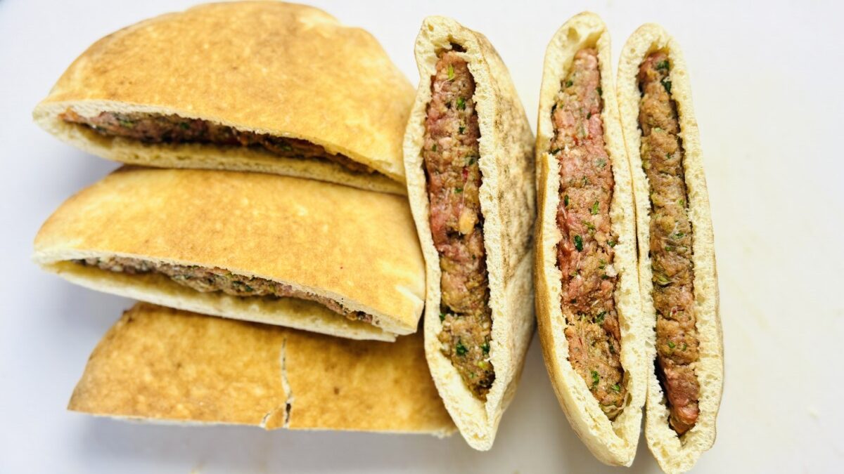 Multiple pita bread halves filled with spiced meat mixture, arranged on a tray and ready to be grilled for Arayes.