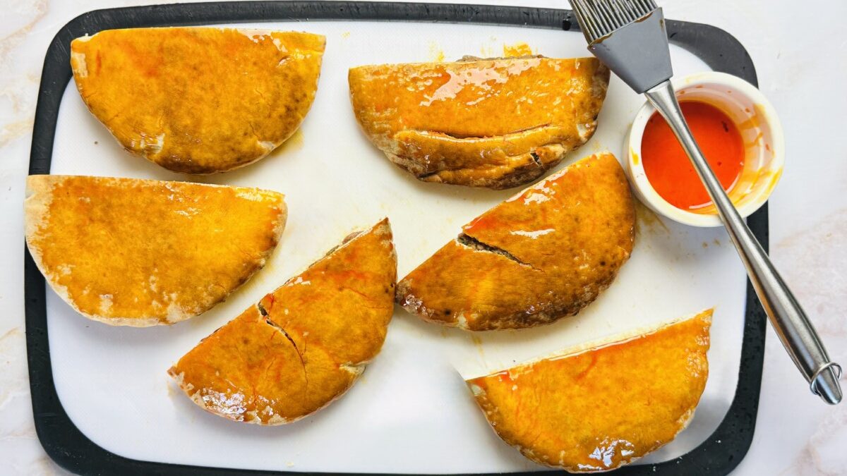 Stuffed pita halves being brushed with chili oil, ready to be grilled for spicy, flavorful Arayes.