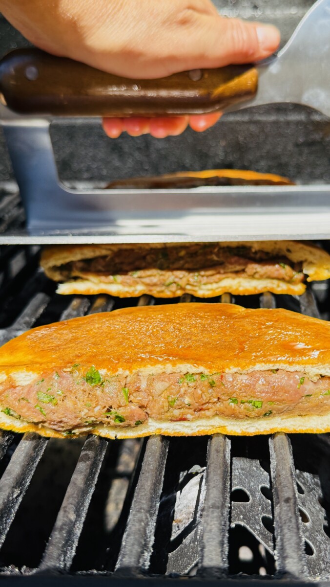 Arayes on the grill being pressed down with a spatula or grill weight to ensure even cooking and prevent shrinking.
