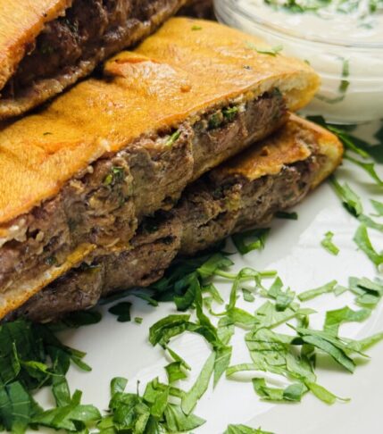 Golden grilled Arayes served on a plate with a creamy yogurt dip and garnished with herbs.