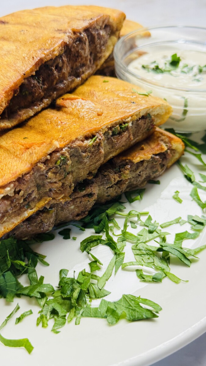 Golden grilled Arayes served on a plate with a creamy yogurt dip and garnished with herbs.