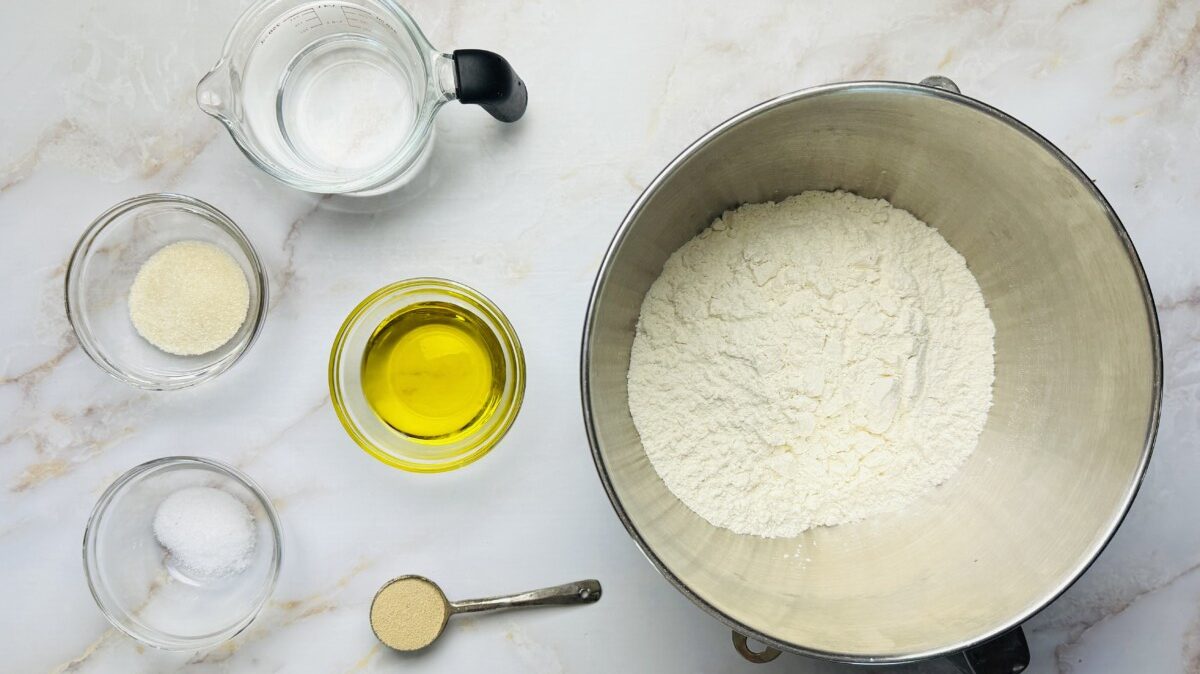 Dough ingredients measured and ready to mix, including flour, yeast, olive oil, sugar, and warm water in bowls.