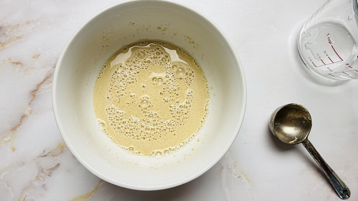 Foamy, bubbly activated yeast in a small bowl, ready to be added to dough mixture.