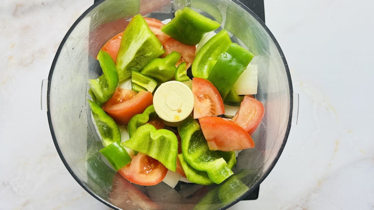 Large chunks of tomato, onion, bell pepper, garlic, and jalapeño in a food processor before blending.