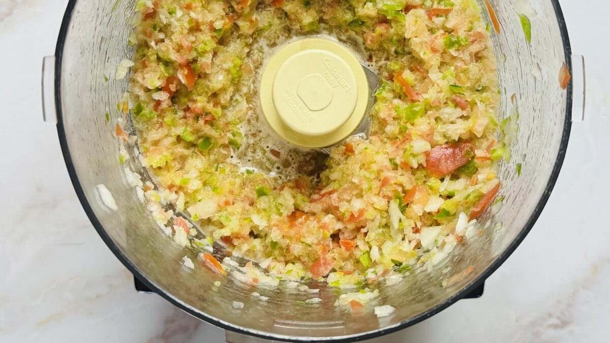 Finely chopped tomato, onion, and pepper mixture inside a food processor, ready for straining.