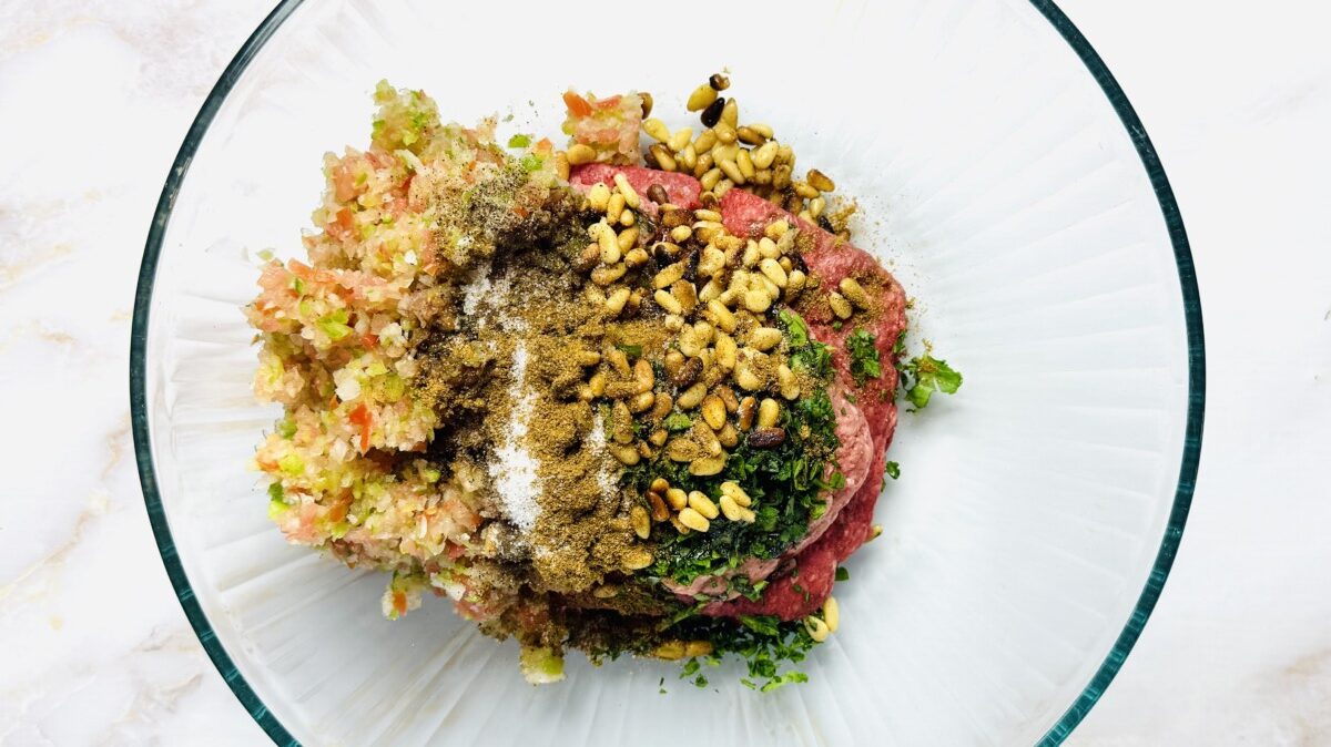 Strained vegetable mixture being added to a bowl of ground beef and lamb for sfeeha filling.