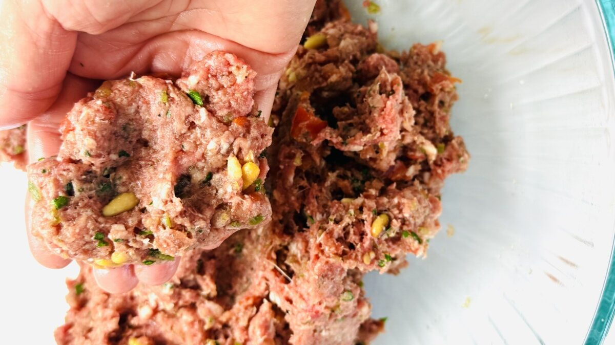 A hand holding a portion of the sfeeha meat mixture above a bowl, showing its texture and consistency.