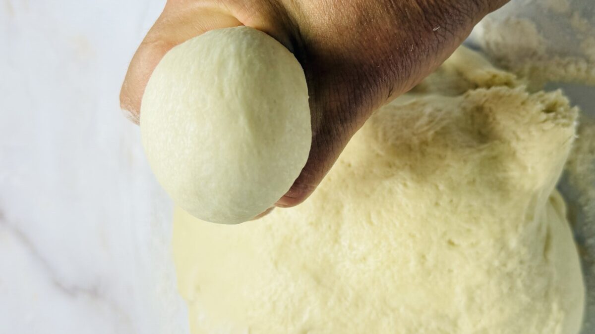 Hands shaping risen dough into smooth balls, ready for resting before shaping into sfeeha.