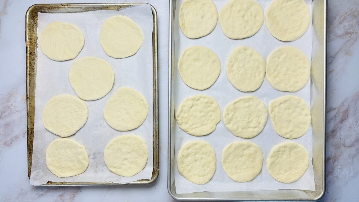 Fingers pressing dough balls into round, flat circles directly on parchment paper.
