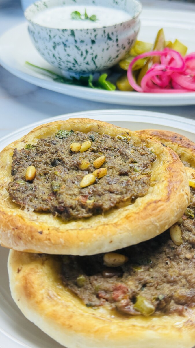 A few baked sfeeha arranged on a serving platter with yogurt sauce and pickled vegetables on the side.
