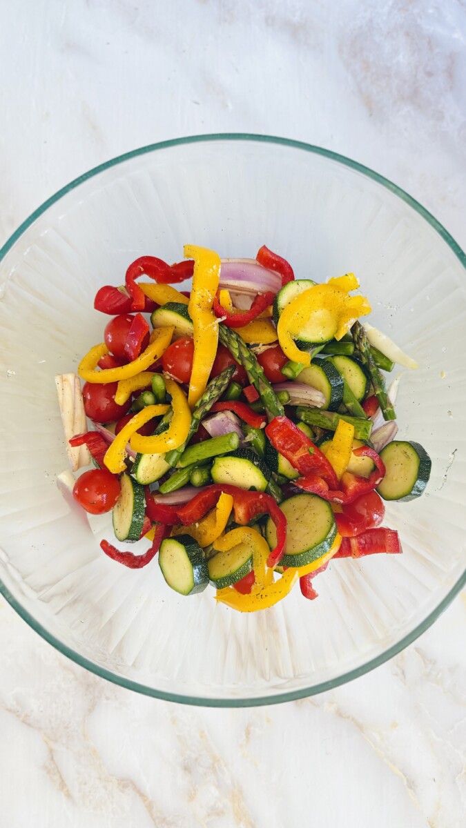 Sliced zucchini, bell peppers, tomatoes, and shallots tossed with herb marinade in a large mixing bowl