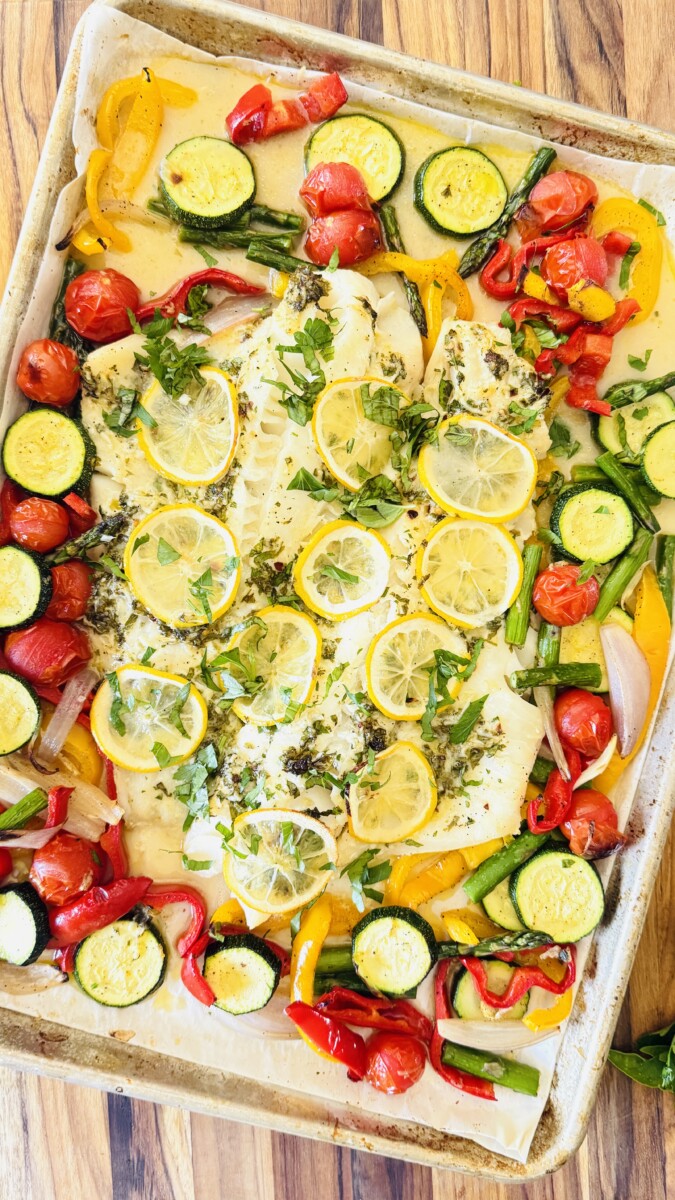 Baked cod fillets served with roasted vegetables and fresh herbs on a platter, garnished with lemon