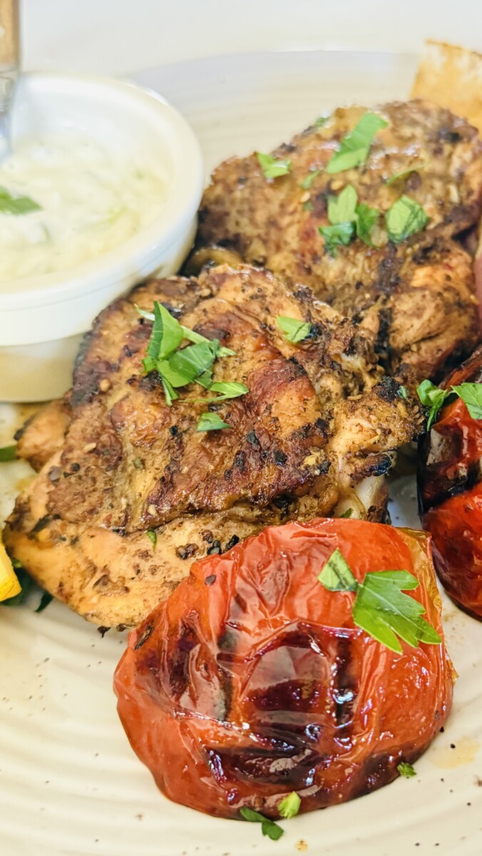 ndividual plate with grilled chicken thigh, roasted tomatoes and onions, and a dollop of yogurt sauce.