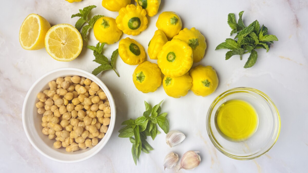 “Fresh ingredients for sautéed summer squash recipe: yellow squash, chickpeas, garlic, lemon, olive oil, cumin, and fresh herbs.