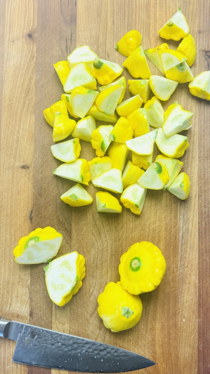 Quartered yellow summer squash on a cutting board, ready for sautéing.