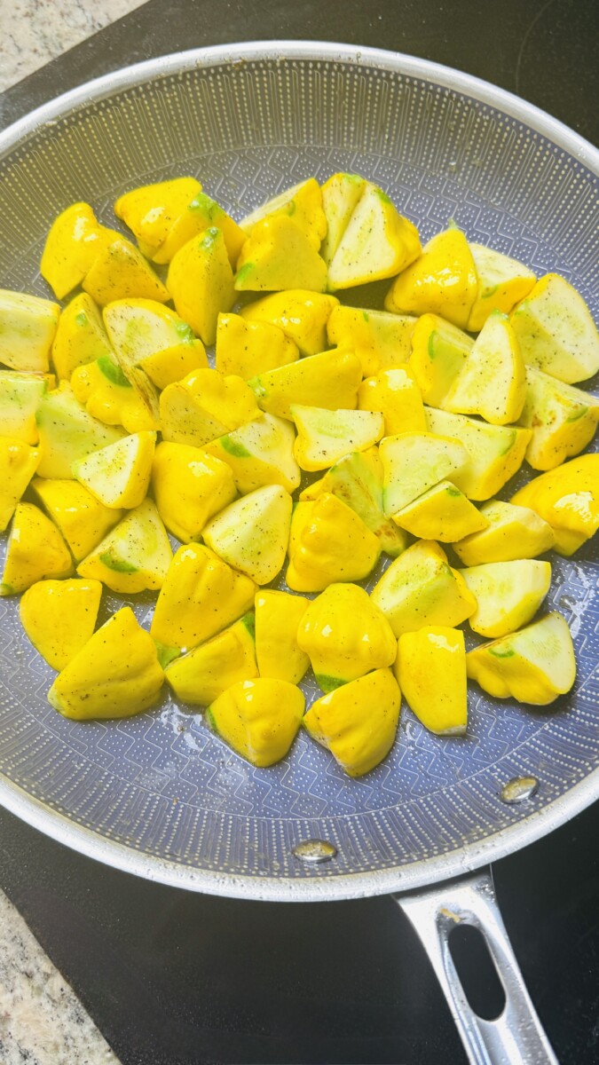 Quartered yellow squash sautéing in olive oil in a skillet.