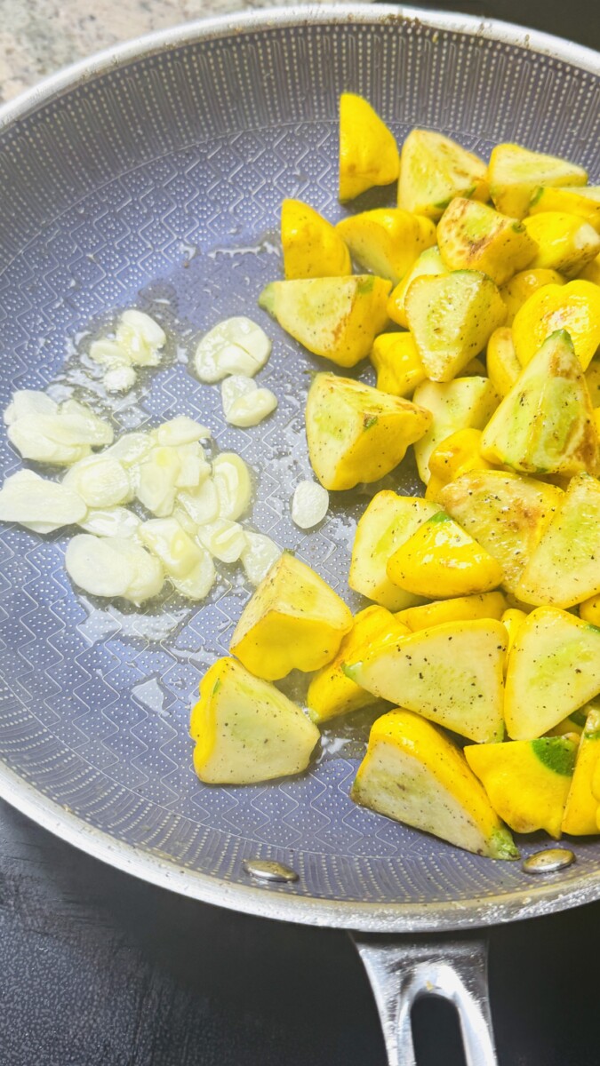 Sautéed squash pushed to the side of the skillet with minced garlic and cumin sizzling next to it.