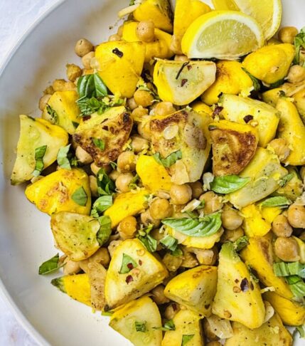 Finished sautéed summer squash with chickpeas, garnished with fresh herbs and a drizzle of olive oil, served warm.