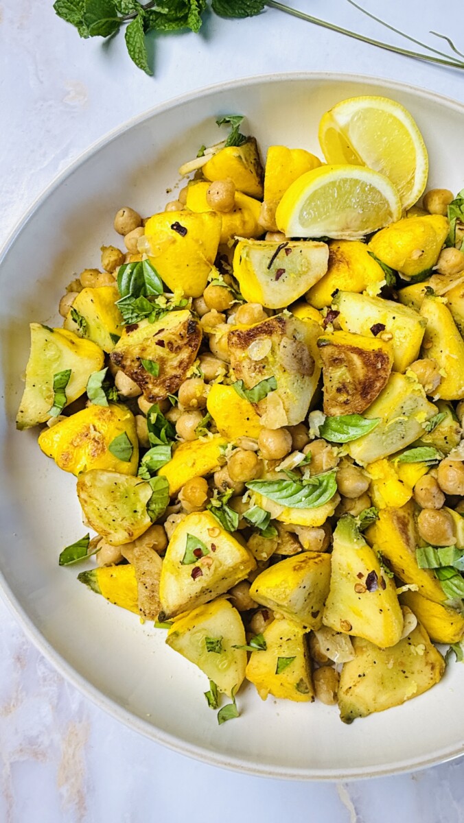 Finished sautéed summer squash with chickpeas, garnished with fresh herbs and a drizzle of olive oil, served warm.