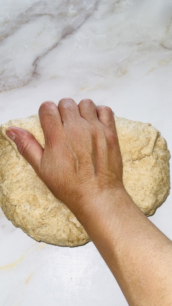 Using the palm of the hand to press pita bread dough while kneading.